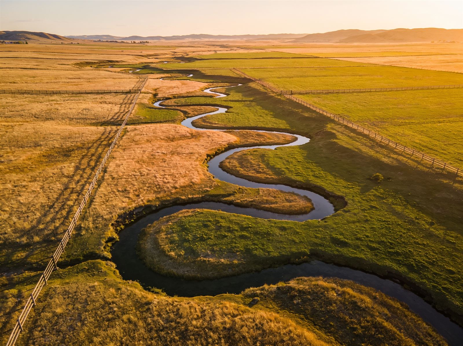 Aerial view of open ranch land with a creek and fence lines at sunset